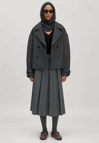 Grijze wollen dubbelgeknoopte zeemanjas, geribbelde grijze sjaal, zwarte bodysuit, geplooide grijze rok, grijze panty en kastanjebruine schoenen met zilveren studs.