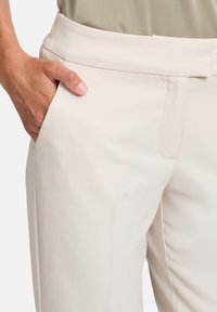 Světlé béžové kalhoty s hladkým povrchem, bočními kapsami a plochým pasem. Disponují čistými liniemi s minimem švů.