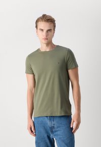 Olivgrünes T-Shirt mit Rundhalsausschnitt, kurzen Ärmeln und einem kleinen Logo-Akzent auf der Brust. Der Stoff wirkt weich und lässig.