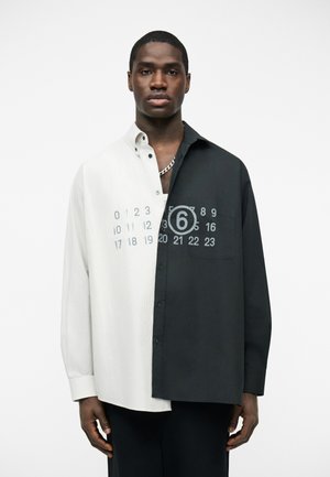 Mand iført en halv-hvid, halv-sort skjorte med knapper, hvor kalendernumre er trykt på brystet, og tallet seks er cirklet.