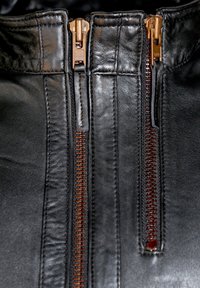 Zwarte leren jack met twee bronzen ritsen en opvallende stiksels langs de kraag en de rits.