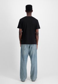 Schwarzes Baumwoll-T-Shirt mit kurzen Ärmeln und Rundhalsausschnitt, kombiniert mit lockeren blauen Jeans aus Denim mit ausgewaschenem Finish und zwei hinteren Taschen.