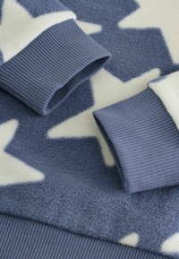 Sinine fliisriide, millel on kreemjas värvuses tähtmuster, tumedama sinise ribaga cuffs ja hem, rõhutades tekstuuri ja kontrasti.