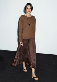 Braunes Langarmoberteil, gefalteter brauner Maxirock und braune Flip-Flops; minimalistisches Design, weicher Stoff, fließende Silhouette.