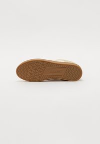 Suola in gomma marrone con un motivo di grip testurizzato; presenta una parte superiore liscia di un beige chiaro con perforazioni per la traspirabilità.