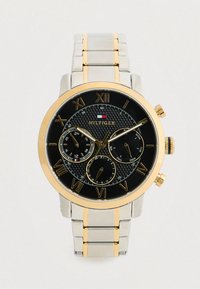 Férfi Tommy Hilfiger karóra fekete tárcsával, arany római számokkal, három alsó számlappal, ezüst és arany fém szíjjal.