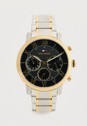 Reloj de pulsera para hombre de Tommy Hilfiger con dial negro, números romanos dorados, tres subdiales y pulsera de metal plateado y dorado.