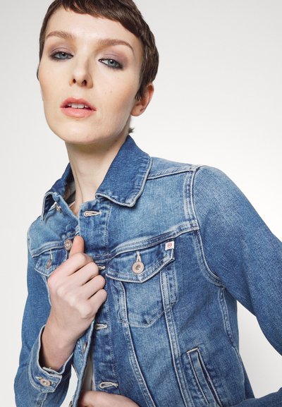 Veste en denim bleu clair avec une coupe classique, fermeture à bouton et poches poitrine. Le tissu a une légère texture avec des zones décolorées.