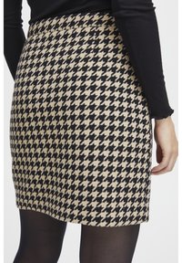 Spódnica w czarno-beżowy wzór houndstooth o dopasowanej sylwetce, gładkiej fakturze i z paskiem w talii, sięgająca do połowy uda.
