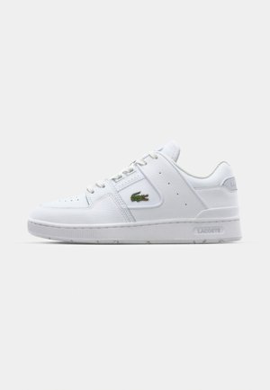 Baskets de sport blanches en cuir texturé, avec une semelle plate, un système de laçage et un logo Lacoste vert sur le côté.
