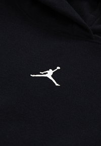 Hanorac negru cu un logo Jumpman alb proeminent. Materialul este moale, tricotat și texturat, având un design clasic și glugă.