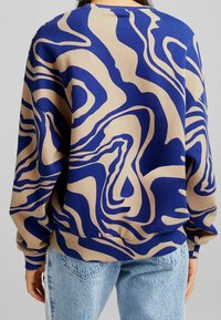 Sweatshirt med en blå och beige abstrakt mönster, med ribbade ärmslut och nederkant, tillverkad av ett mjukt, texturerat tyg.