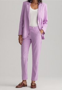 Lilacový lněný blazer s odpovídajícími kalhotami na míru, s jediným knoflíkovým uzávěrem a bočními kapsami; nošený přes bílý ribbed top.