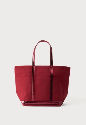 Borsa tote rossa con manici e bordi con paillettes lucenti alla base, in piedi su uno sfondo bianco.