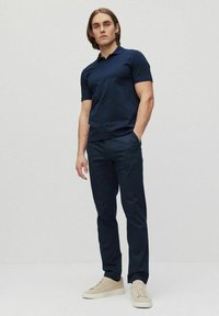 Marineblauw poloshirt met korte mouwen en een smal ontwerp, gecombineerd met donkerblauwe broek en beige sneakers. Glad materiaal met een klassieke kraag.