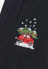 Sort ribbet stof med en rød broderet bil, der bærer et grønt juletræ, snefnug i hvidt ovenfor og sne under bilen.