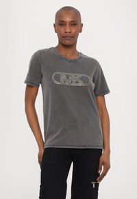 Camiseta gris de manga corta con un cuello redondeado y un logo "CMK" con tachuelas en el frente. La tela tiene una textura suave y ligeramente desgastada.