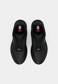 Black sneakers with a textured leather upper, round toe, and flat laces. Features a stripe logo in red, white, and blue on the tongue.