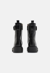 Botas de tobillo de cuero negro con un acabado suave, que cuentan con una cremallera lateral, un tirador en la parte posterior y una suela resistente y texturizada.