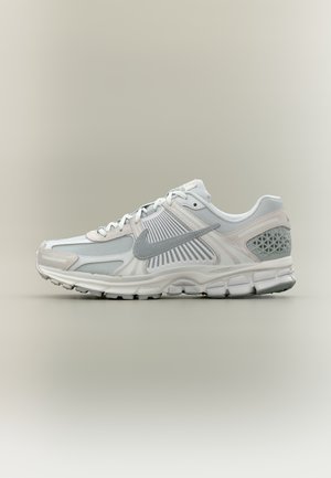 Chaussure de course Nike blanche et grise avec des superpositions en mesh et synthétiques, logo swoosh gris, semelle amortie et support talon texturé.