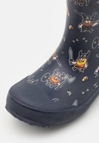 Blå gummistövel med en texturerad yta, prydd med tecknade vikingakaraktärer, vapen och symboler i olika färger. Rundad tådesign.