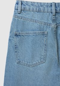 Jeans in denim blu chiaro con tasca posteriore con cuciture visibili e passanti per cintura su uno sfondo semplice.