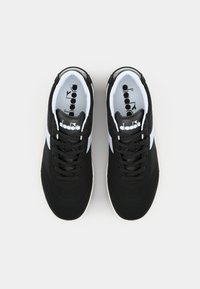 Baskets de sport noires avec des accents blancs, tige en textile lisse, bout rond et lacets plats. Présente une marque sur la languette et le côté.