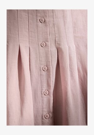 Tissu rose clair avec des plis verticaux et une rangée centrale de boutons ronds assortis cousus avec quatre trous.