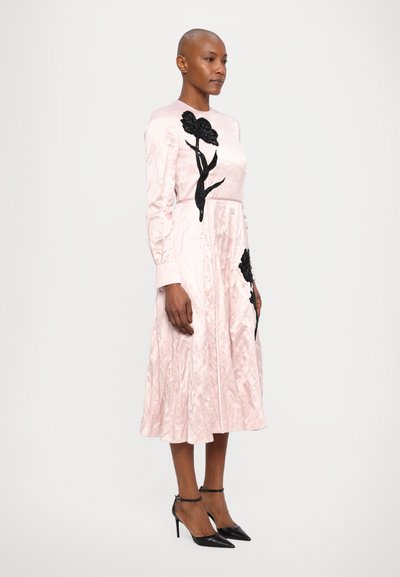 Pink satin dress with long sleeves, floral black embroidery, flowing skirt, and pointed black heels. Smooth texture with gathered detail.