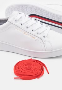Bílé tenisky Tommy Hilfiger s bílými tkaničkami, navinuté červené tkaničky vpředu a podrážkou s červenými, bílými a modrými pruhy.