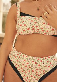 Blommig baddräkt i två delar med grön bas, röda körsbär och vita blommor, svart kant och fyrkantig halsringning på toppen.