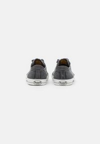 Gray canvas shoes with white rubber soles and contrasting stitching. Features padded heel and branding on the back. Low-top design.