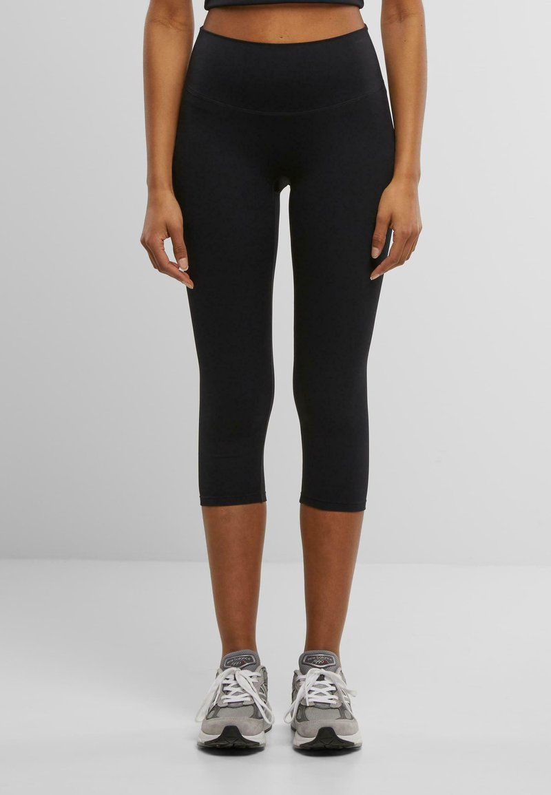 Black capri leggings made from a stretchy, smooth fabric with a high waist design. Paired with gray athletic shoes.
