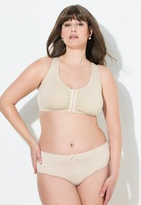 Beige draadloze bh met een geplooid midden en sluiting aan de voorkant. Bijpassende beige slip met een kleine strikaccent. Glad textuur van de stof, eenvoudig ontwerp.