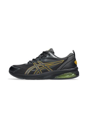 Zapatilla deportiva negra con upper de malla, líneas de acento amarillas y amortiguación de gel verde en la suela. Presenta una punta redondeada y detalles texturizados.