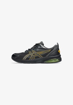 Baskets de sport noires avec tige en mailles, lignes d'accent jaune et semelle avec amorti en gel vert. Présentent un bout arrondi et des détails texturés.