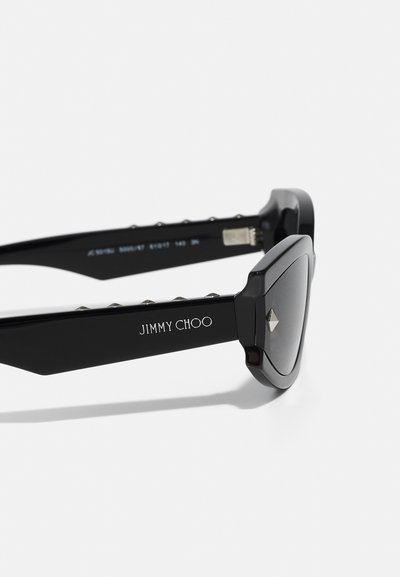 Mustad mustikad prillid nurksete disainiga, metallist aksessuaarid kaitsetel ning graveeritud brändi nimi "JIMMY CHOO". Tumedalt toonitud objektiivid.