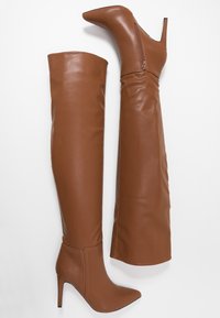 Botas marrones de tacón alto, hasta la rodilla, hechas de cuero sintético suave, con punta afilada y cremallera lateral. Diseño elegante y ajustado.