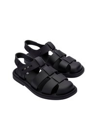 Sandales noires ayant un design à lanières avec de larges sections plates, une semelle épaisse et une lanière de cheville ajustable pour un maintien sécurisé.