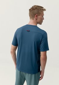Krátký rukáv sportovního trička v tmavě modré barvě, vyrobeného z lehkého materiálu, obsahuje větrací otvor na zádech a kontrastní červený detail na krku.