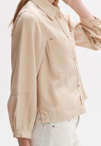 Beige overhemd met knopen, lichtgewicht stof, ontspannen pasvorm, enkele borstzak en opgerolde mouwen met zijsplitten.