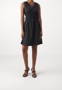 Svart ärmlös klänning med samlad midja, V-ringning och utsvängd kjol. Bärs med svarta strappy högklackade sandaler.