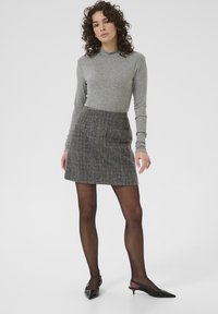 Gray long-sleeve top paired with a patterned mini skirt featuring a plaid design in black and brown, complemented by sheer black tights and pointed shoes.