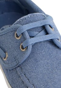 Zapatillas de lona azules con ojetes metálicos redondos, cordones en contraste y una superficie de tela texturizada con costuras visibles.
