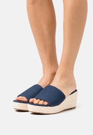 Sandales compensées en denim avec un design à deux bandes, présentant une semelle tissée texturée. La couleur est bleu foncé avec une base tissée de couleur naturelle.