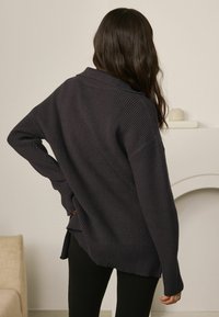 Maglione oversize grigio scuro con texture a costine, maniche lunghe e colletto. Presenta un orlo spaccato e una vestibilità comoda.