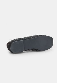 Suela de zapato negra con superficie de goma texturizada y tachuelas elevadas para mayor agarre, con punta redondeada y diseño de tacón liso y plano.