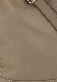 Beige leermateriaal met een gestructureerd oppervlak, voorzien van een zilveren gesp en stikseldetails. Het ontwerp is glad zonder extra patronen.