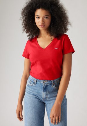 T-shirt en coton rouge avec un col en V et des manches courtes, arborant un petit logo Levi's. Associé à un jeans bleu clair taille haute.