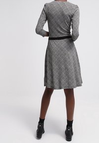 Rutig klänning i svart och vitt med figurnära midja och utsvängd kjol, långa ärmar och ett svart bälte, tillverkad av ett slätt, elastiskt tyg.